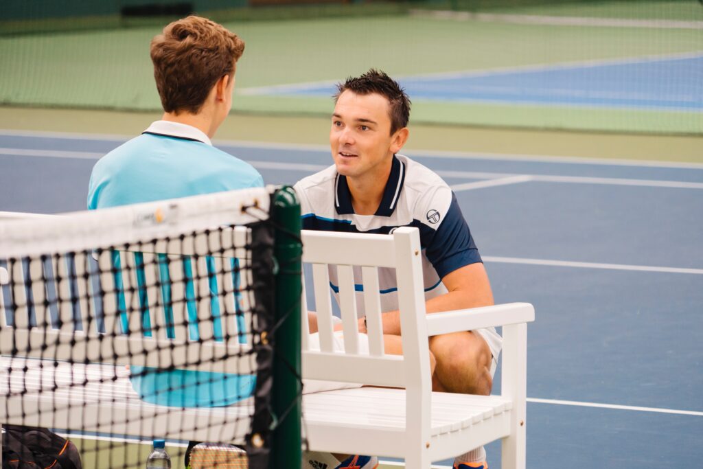 Man geht in die Hocke und redet mit einem mann der vor ihm auf der Bank sitzt