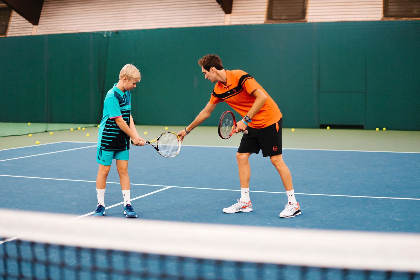 Ein Tennistrainer zeigt seinem Schüler wie er den Schläger halten muss.